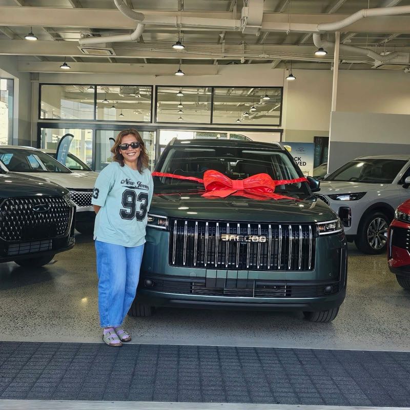 Customer smiling beside their new SUV with a red bow in a dealership